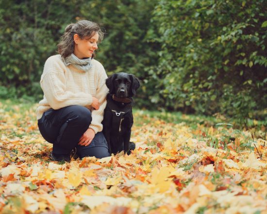Ellie kniet im Herbstlaub neben ihrem schwarzen Hund Enni.